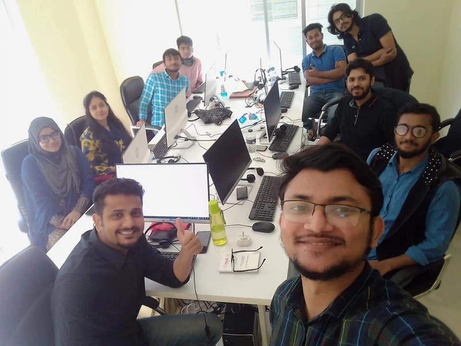 Nine colleagues gathered around a meeting table with laptops open, one screen displaying source code during a review session