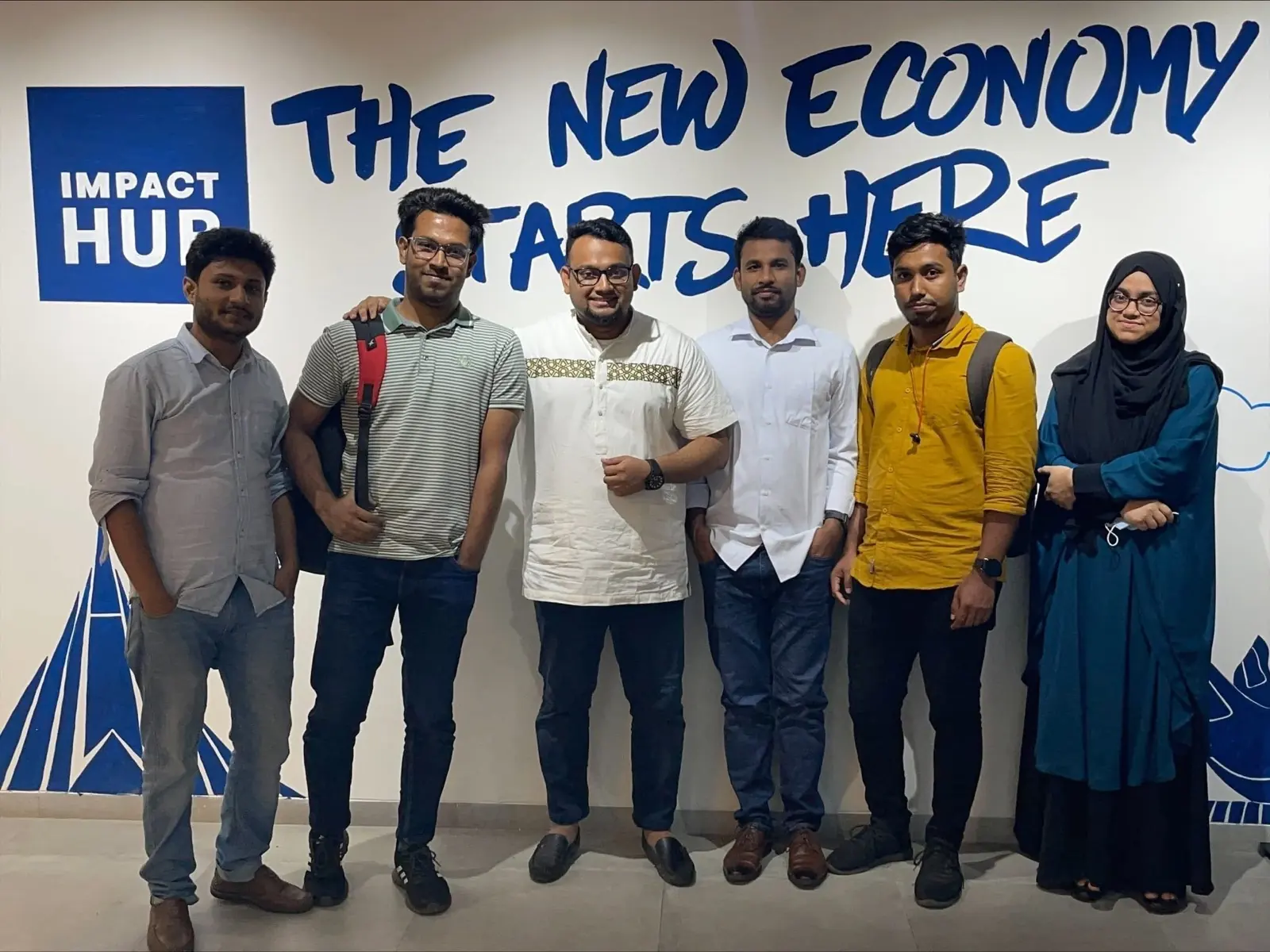 Six colleagues standing in front of a large Impact Hub wall mural reading 'The New Economy Starts Here'